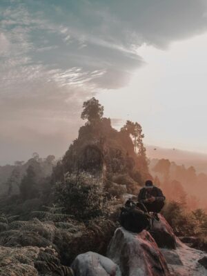 A lone hiker enjoys the serene sunrise on a misty mountain peak, surrounded by breathtaking nature.